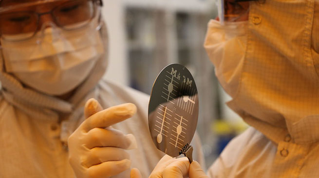 Researchers in bunny suits pointing to fabricated chip